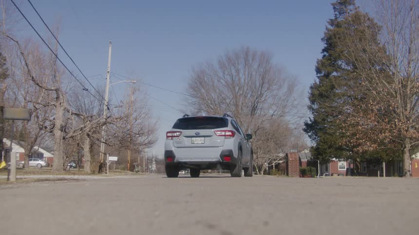 A white automobile is traveling slowly on a neighborhood street