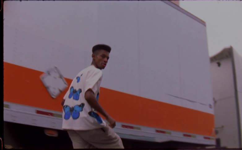 Young man rides a skateboard near a truck parked on the city street caught on vintage film