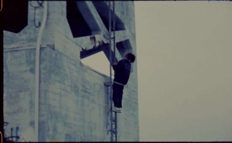 A person climbing up a ladder against a building looks up