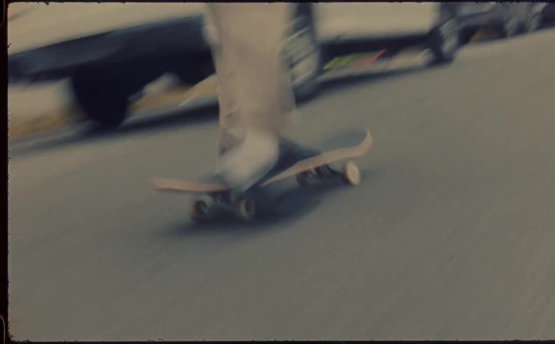 Man with beige pants and black shoes skateboards in the street next to vehicles in the city