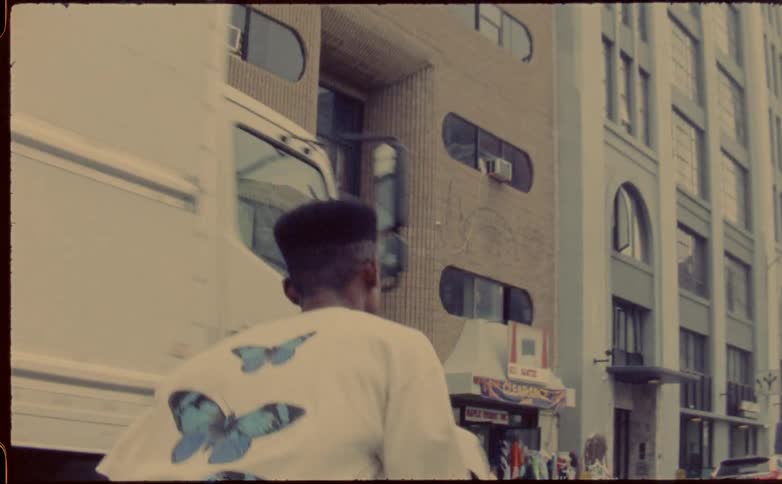Man skateboards down street passing storefronts and a parked truck
