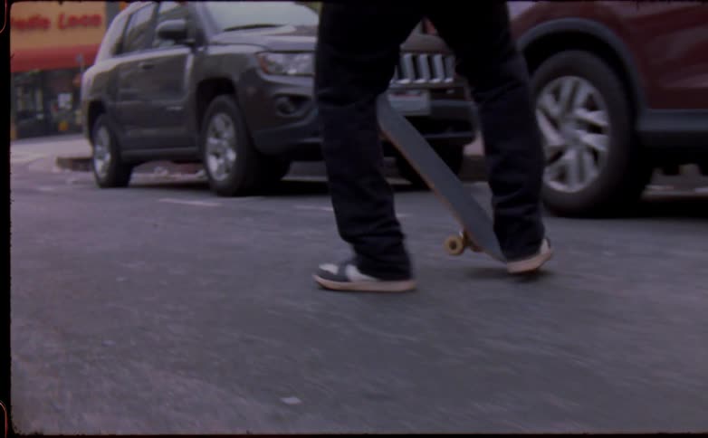Man with black pants and sneakers skateboards in the street