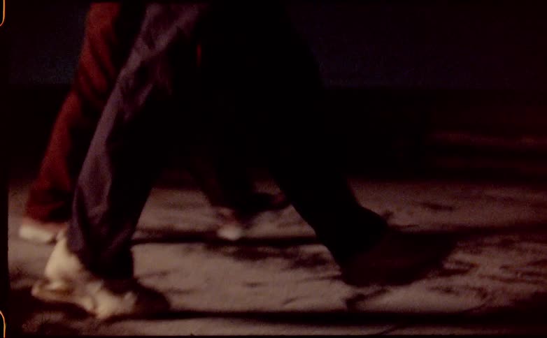 Two people walking in sync on the sidewalk at night