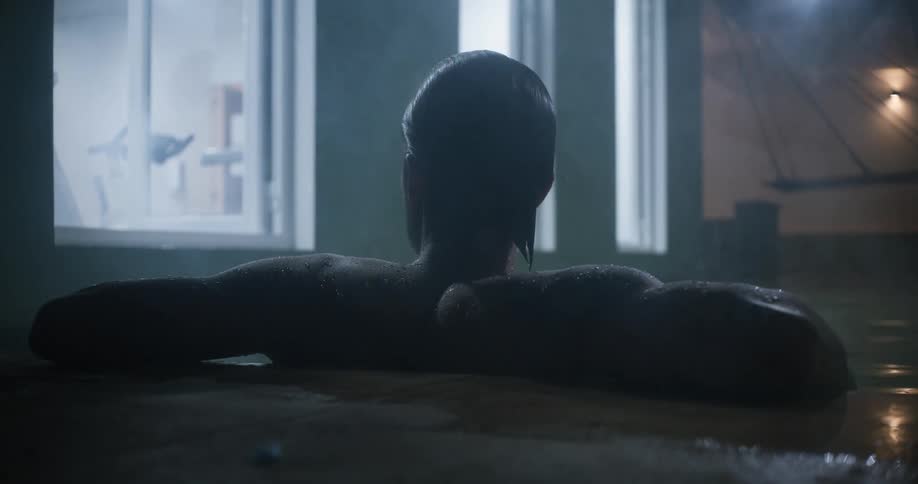 Silhouette of a young man surrounded by steam takes a relaxing bath on a dimly lit hot sauna