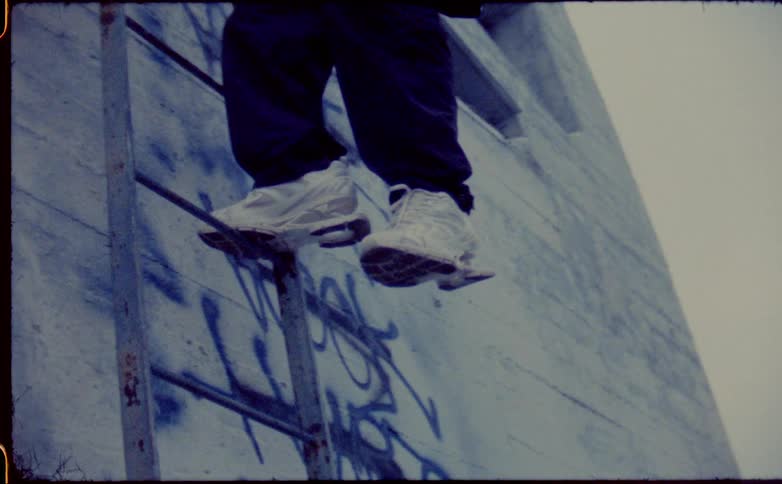 A man hands from a ladder outside a tagged building