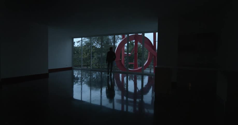 Man walking towards the big glass window indoors in the empty and dark living room