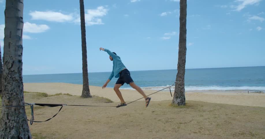 Young man practices walking on a ropewalk in front of a beach