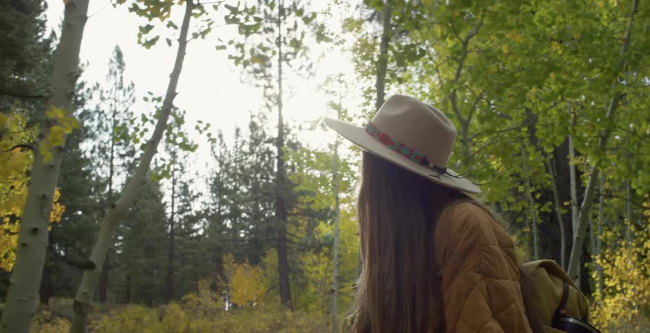 Woman wearing hat and jacket hiking through forest enjoying fall foliage