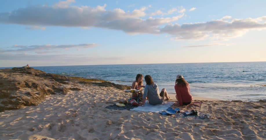 Three female friends sitting on the sand near shoreline at the beach