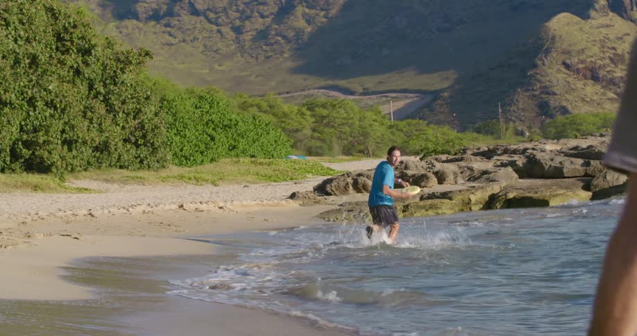 Two young men playing with a frisbee on the coast of a beach close to the mountains