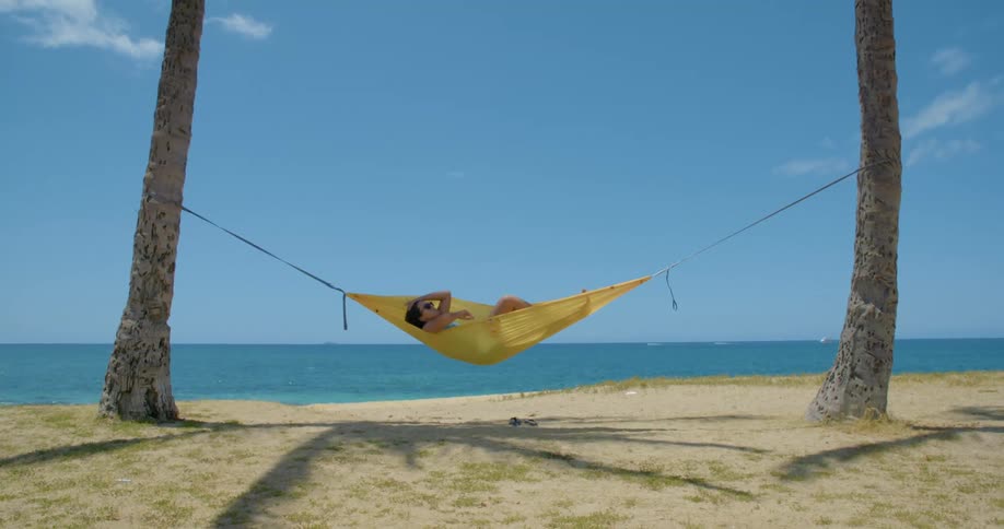 Woman swaying in a yellow hammock tied to palm trees in the tropics