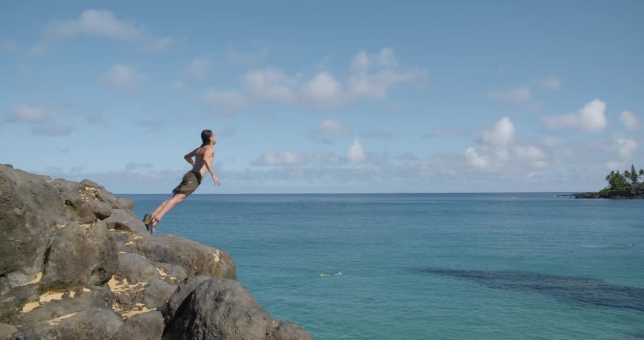 Man jumping off cliff into the ocean at a sunny day