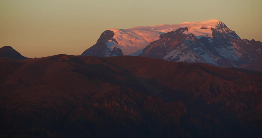 View over a mountain of a snow covered mountain under a clear sky