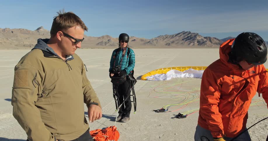Three people are preparing a paragliding machine on a field