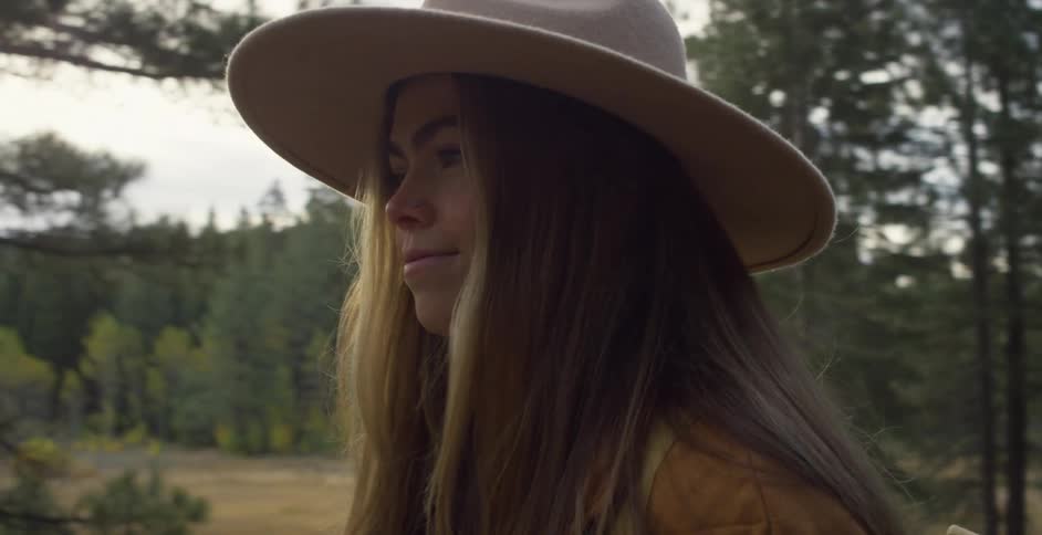 Woman wearing a brimmed hat and carrying a backpack on her back walks on a trail in the forest