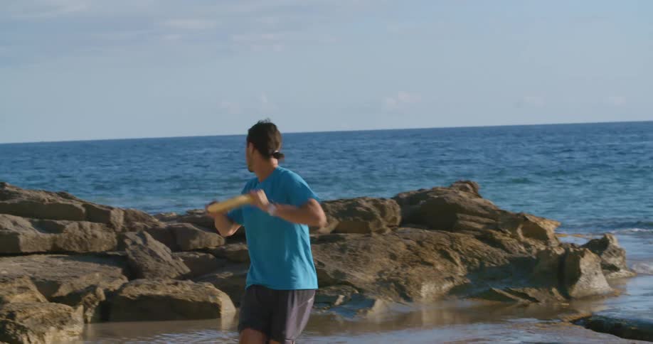 Male in blue shirt playing frisbee at the shoreline near the ocean