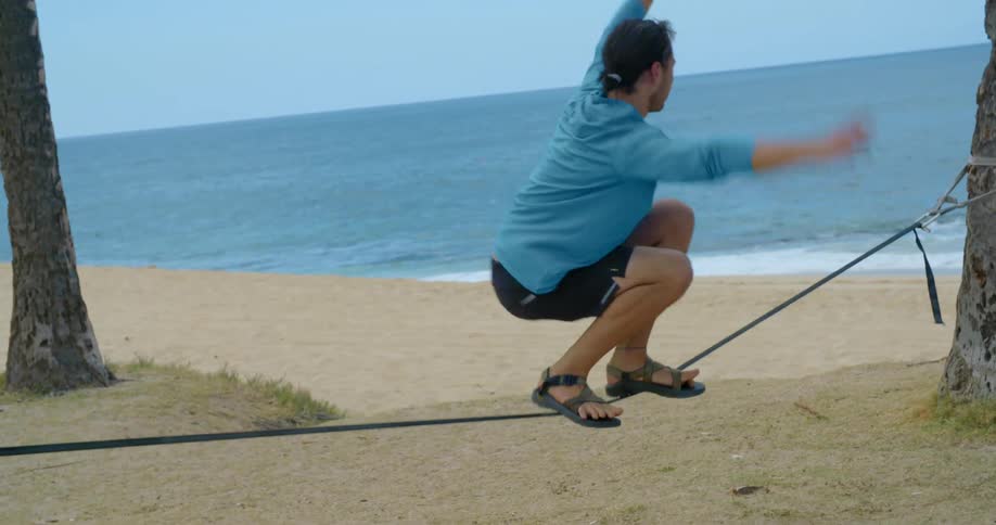 Young man practices jumping on a ropewalk in front of a beach