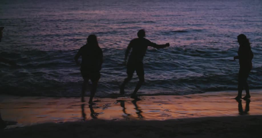 Male celebrating sand crab he caught on beach shoreline at sunset with friends