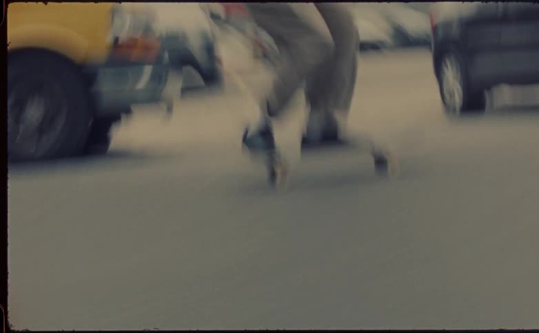 Man with beige pants and black shoes skateboards on highway next to vehicles in the city