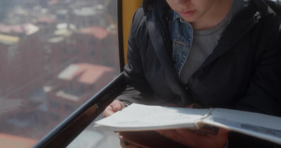 Young woman reading while sitting on the cabin of a cable car over the city