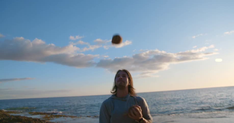 Young happy man juggling coconuts on the beach next to the ocean at sunset