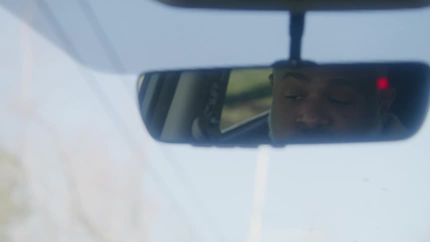 The reflection of a driver in a rearview mirror rubbing his face and shaking his head in frustration