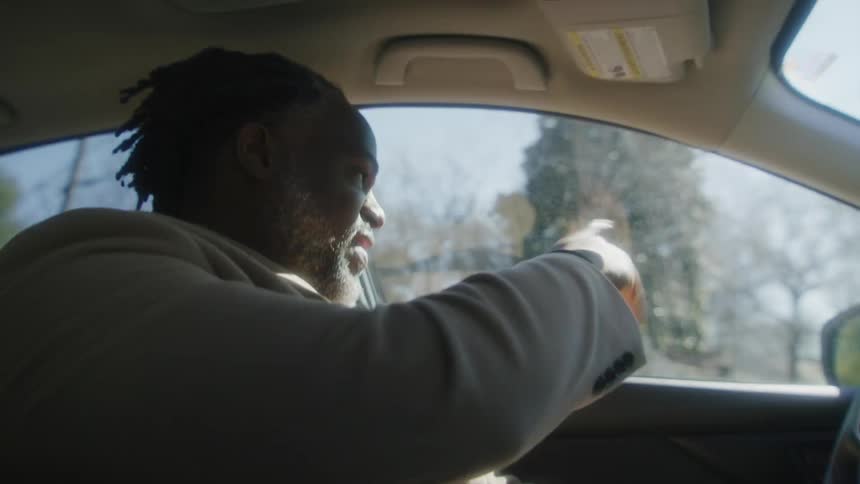 Happy man driving a car on a neighborhood waves at someone in the curb
