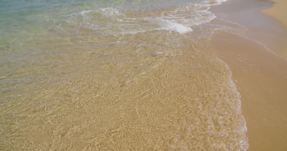 Clear water waves roll over the sand on a beach