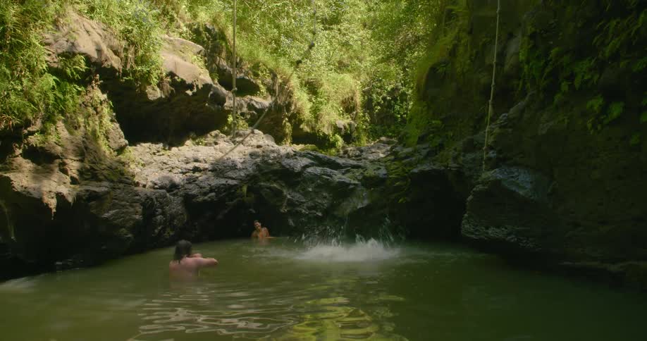 Man swings on a rope over the rocks and lets go and falls into the lake water below in the forest
