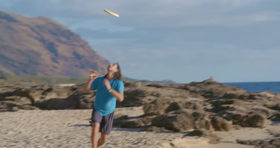A man on a beach runs and catches a frisbee and then throws it