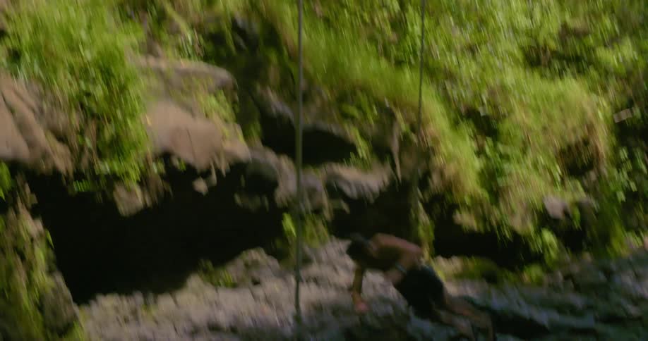 Man wearing shorts jumps off cliff into water in the forest