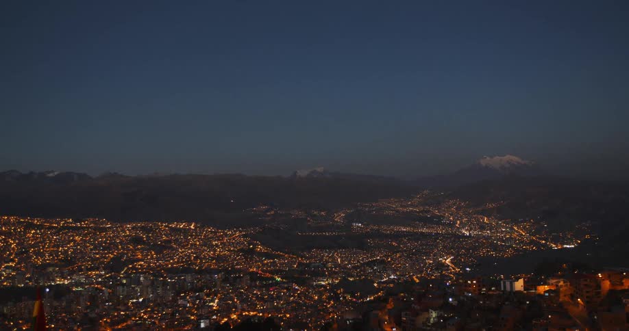 A dense city near mountains is lit up bright at night