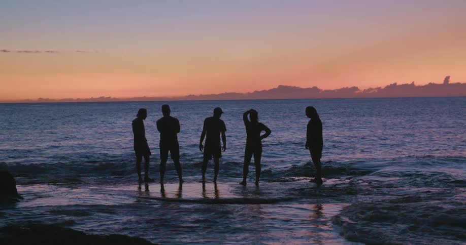 A group of people stand at the beach as the ocean water washes over their feet