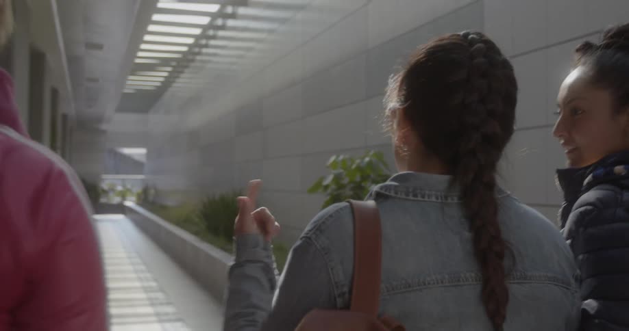 Group of female friends wearng jackets walk down a hallway on a building