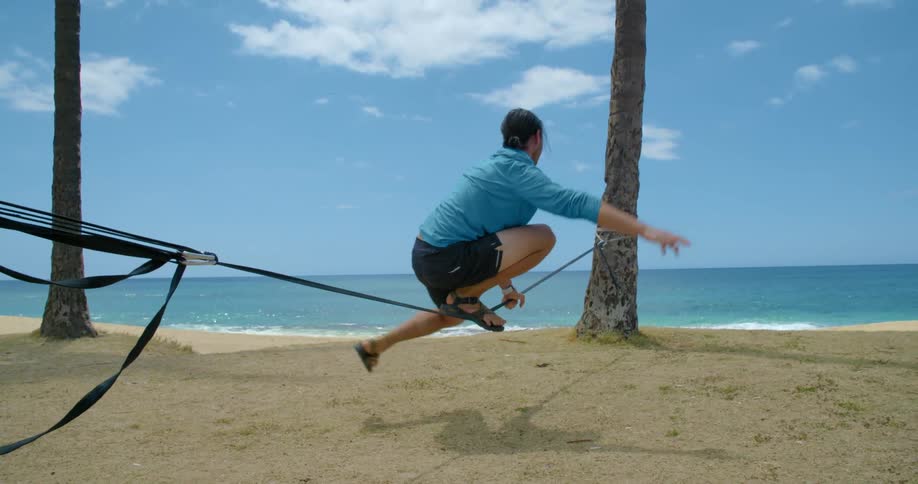A man on a beach performs balancing acts on a tight rope