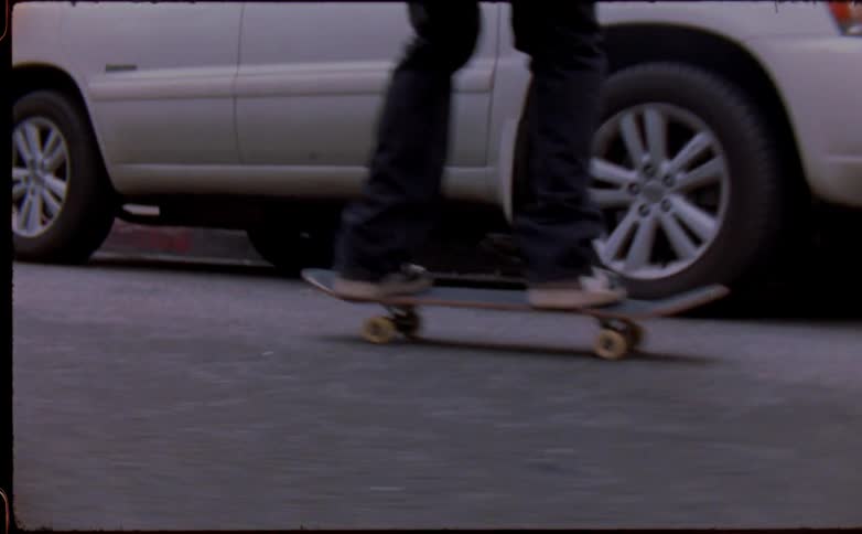 Young man riding a skateboard doing tricks on the city street caught on vintage film
