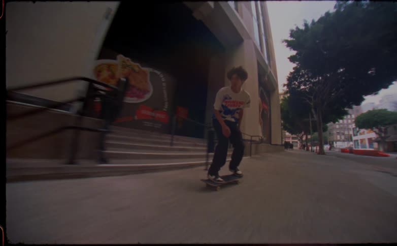 Teen wearing white t shirt and black pants skateboards on sidewalk in city street