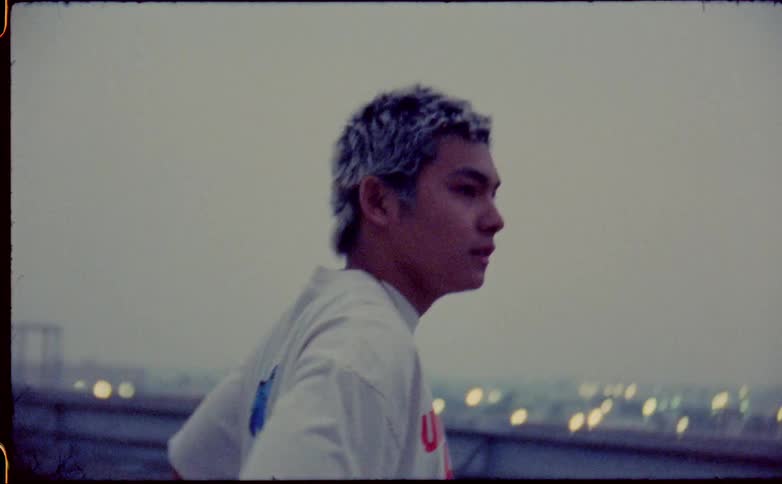 Young man walking on the roof of a building next to the city at evening