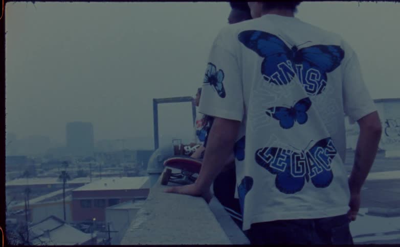 A group of teenagers stand on a rooftop and look over the edge as they talk
