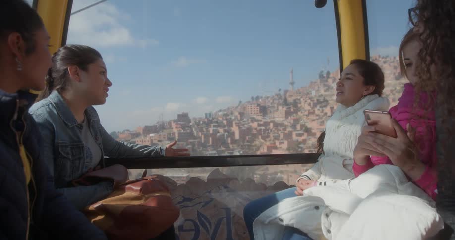 Group of female friends talking and laughing on the a moving cable car over a mountain town