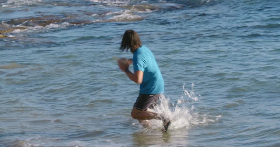 Young man standing on the shallow water on a beach catches a frisbee and throws it back