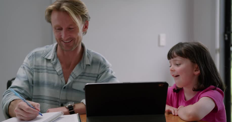 A little girl bites her lip before answering a question her dad smiling as he writes in a notebook