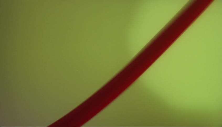 Crimson fluid flows through translucent tube near green tinted background
