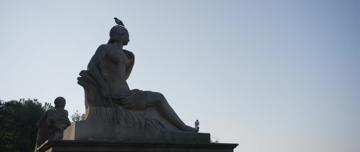 Pigeons perched on a statue of a seated woman overlooking Barcelona
