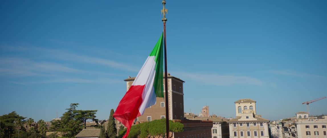 Italian flag hanging from a flag post waving in the wind in front of the city skyline