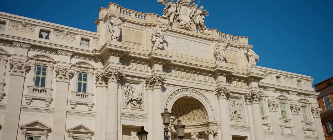 Black bird flies toward ground near architecturally detailed landmark building under a blue sky
