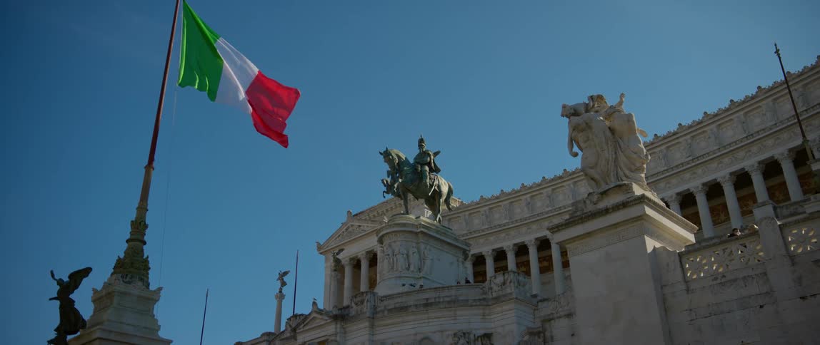 An italian flag flies in front of a historical building with sculptures
