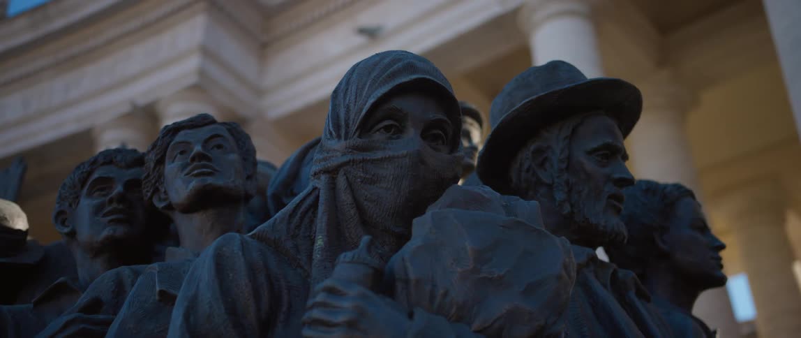 Close up of the heads of a sculpture in front of a classical building