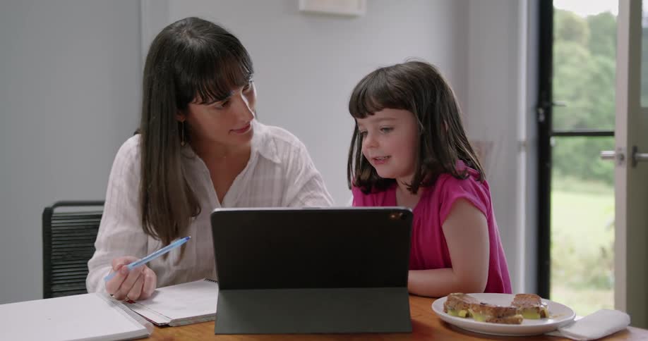 A mom smiles and encourages her daughter as she learns at home