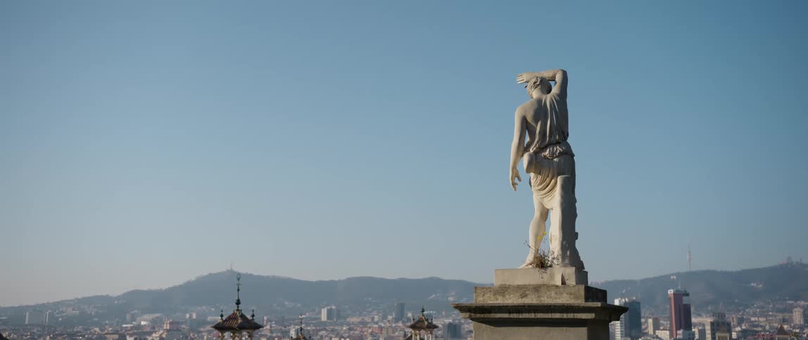 A sculpture of a man sits on a tall pedestal above Barcelona